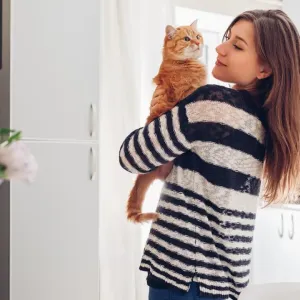 Une jeune femme tient un chat roux dans ses bras et le regarde tendrement dans une cuisine lumineuse.