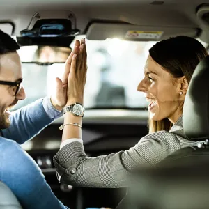 Un homme et une femme souriants se font un high-five à l'intérieur d'une voiture, vus depuis l'arrière.