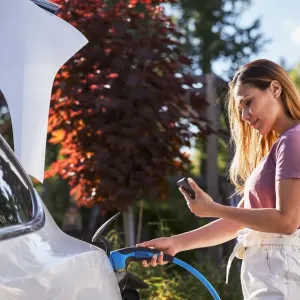 Une femme branche sa voiture électrique et regarde son téléphone.