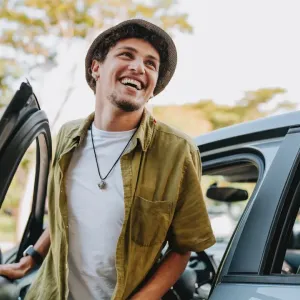 un jeune homme souriant sort de sa voiture.