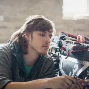 Un jeune homme aux cheveux longs travaille méticuleusement sur les détails d'une moto dans un garage.