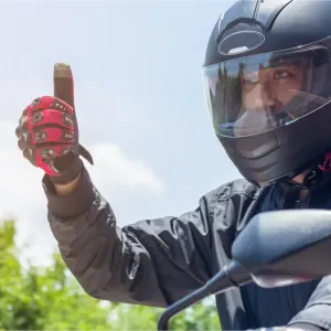 Un motard casqué avec des gants rouges lève le pouce, signifiant que tout va bien.