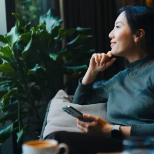 Femme pensive assise avec son téléphone, regardant par la fenêtre.