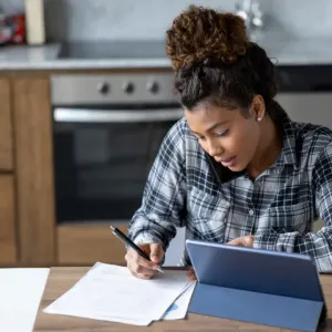 Femme en chemise à carreaux écrivant sur des papiers et téléphonant.