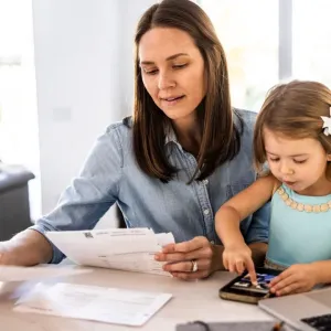 Une mère et sa petite fille sont assises à une table, la mère examinant des documents et l'enfant jouant avec un téléphone.