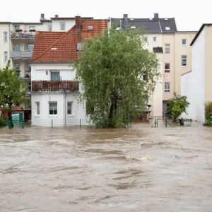 Inondation majeure : l'eau boueuse et agitée submerge la rue devant une ligne d'immeubles résidentiels.