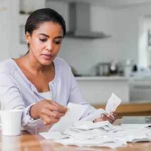 Femme assise à une table avec son ordinateur portable, triant et examinant une pile de reçus ou de factures.