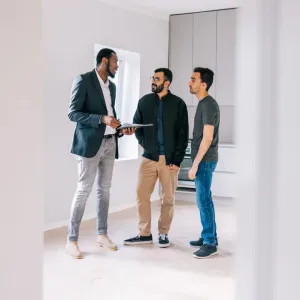 Un agent immobilier et deux clients discutent dans une cuisine minimaliste et vide.