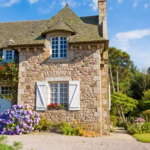 Une charmante maison de campagne bretonne en pierres avec des hortensias bleus.
