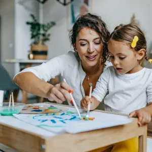 Une mère et sa jeune fille font de la peinture sur papier, assises à une petite table.
