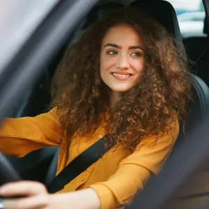 Une jeune conductrice souriante au volant de sa voiture.