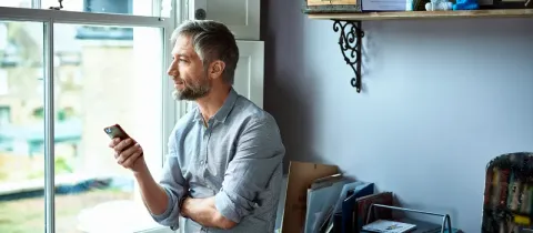 Un homme discute avec une personne via son téléphone portable dans un salon lumineux.