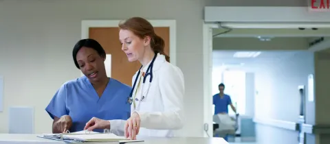 Deux soignantes discutent dans un couloir d’hôpital.