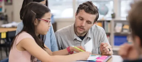 Un homme explique une leçon à une petite fille assise à côté de lui en classe.