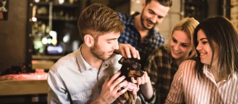 Un groupe d'amis souriants regarde un petit chien noir et marron tenu par un jeune homme.