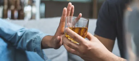 Une main repousse un verre d'alcool offert par une autre main.