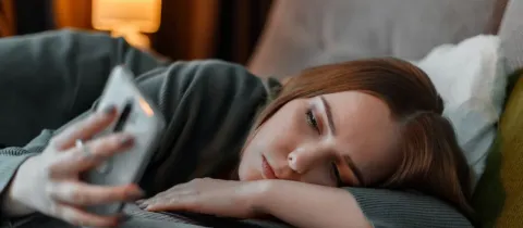 Une jeune femme est allongée, l'air pensif, regardant son téléphone portable.