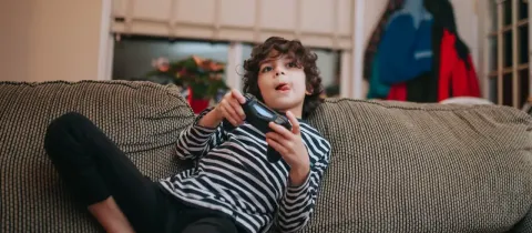 Un jeune garçon est assis sur un canapé, jouant à un jeu vidéo avec une manette.