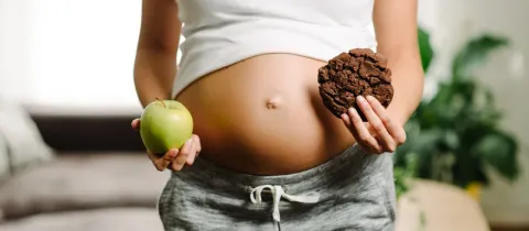 Une femme enceinte tient une pomme verte dans une main et un cookie dans l'autre.