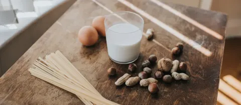 Des œufs, des pâtes, des noix et un verre de lait sont disposés sur une table en bois.