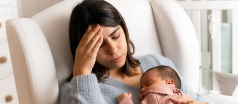 Une jeune mère l'air préoccupé tient son bébé endormi dans ses bras.