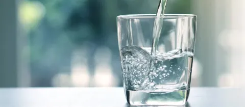 Un jet d'eau fraîche remplit un verre transparent, créant des bulles, avec un fond flou verdoyant.