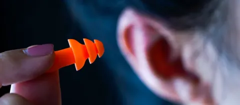 Gros plan d'une main insérant un bouchon d'oreille orange dans une oreille, pour la protection auditive.