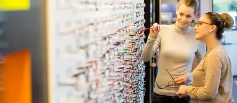 Deux femmes choisissent des lunettes sur un présentoir mural dans un magasin d'optique.
