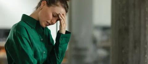 Une jeune femme aux cheveux attachés, vêtue d'une chemise verte, tient sa tête l'air affligé.