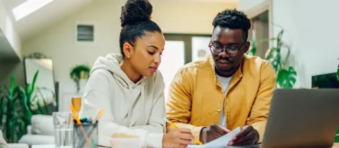 Jeune couple discutant des documents et utilisant un ordinateur portable à la maison.