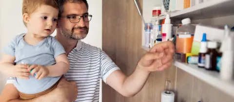 Un père et son enfant en bas âge cherchent des médicaments dans une armoire à pharmacie.