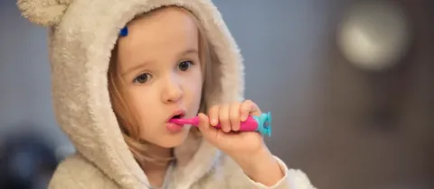 Petite fille brossant ses dents, portant un peignoir à capuche d'animal.