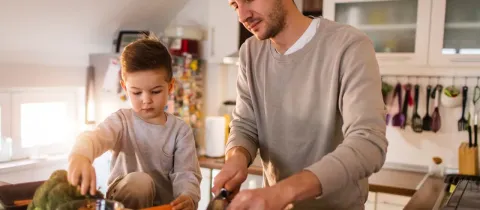 Un père et son jeune enfant coupent des légumes ensemble dans la cuisine.
