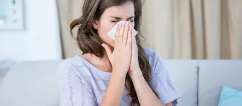 Une femme éternue dans un mouchoir, les yeux fermés, potentiellement liée à une congestion nasale ou une rhinite allergique.