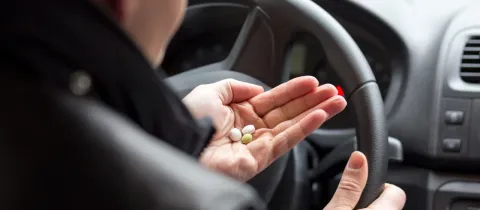 Gros plan sur une main tenant des pilules multicolores près du volant d'une voiture.