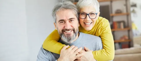 Un couple de personnes âgées souriantes, la femme étreignant l'homme par derrière.