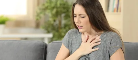 Une femme à la maison, visiblement mal à l'aise, se tenant la poitrine avec une expression de douleur.