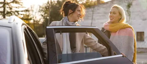Deux femmes souriantes près d'une voiture, l'une ouvrant la portière.