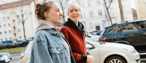 Une mère et sa fille parlent devant des voitures.