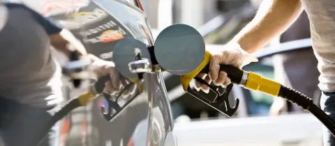 Une main gantée insère un pistolet de pompe à essence dans le réservoir d'une voiture grise, en train de faire le plein.