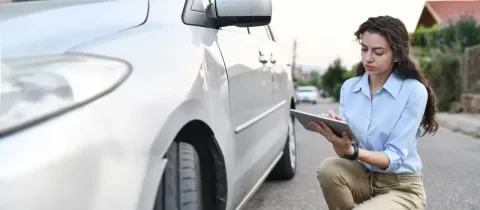 Une femme à genoux à côté d'une voiture, tenant une tablette dans ses mains.