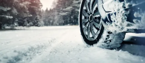 Un pneu de voiture enneigé est visible sur une route couverte de neige, avec des arbres en arrière-plan.