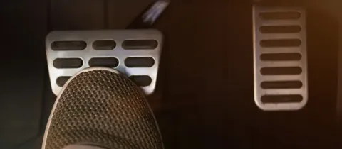 Un pied portant une chaussure grise est posé sur la pédale de frein d'une voiture, à côté de l'accélérateur.