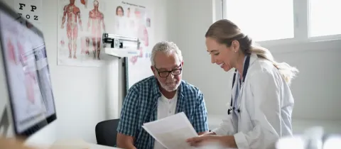 Un médecin souriant et un homme âgé examinent des documents dans un bureau médical.