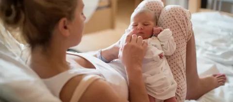Une mère tient son nouveau-né endormi dans ses bras, allongée.