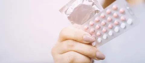 Gros plan sur une main tenant un préservatif et une plaquette de pilules contraceptives.