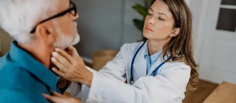 Une femme médecin examine le cou d'un homme âgé avec une barbe.