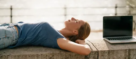 Une femme détendue allongée sur un mur en pierre avec un ordinateur portable à côté.