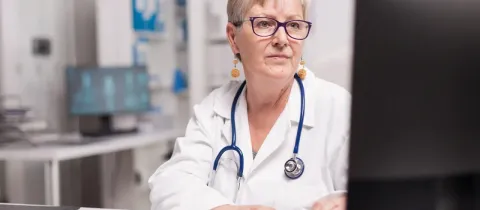 Une femme médecin âgée avec un stéthoscope travaille sur un ordinateur au cabinet.