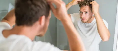 Un homme regardant son reflet dans un miroir, ajustant ses cheveux.